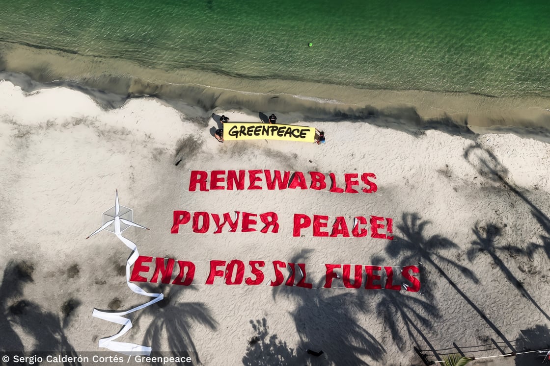 Foto tirada durante a Conferência de Santa Marta, em que ativistas estendem um banner na praia com a frase “Renewables power peace! End fossil fuels”, que significa em português “As energias renováveis promovem a paz! Acabem com os combustíveis fósseis”.